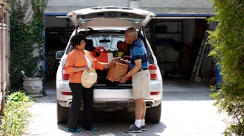 A couple unloads groceries from the back of their SUV.